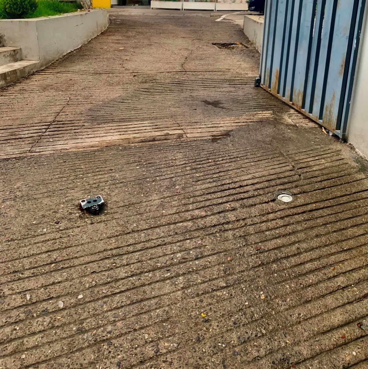 A concrete pathway leading to a building entrance with a metal fence on one side.