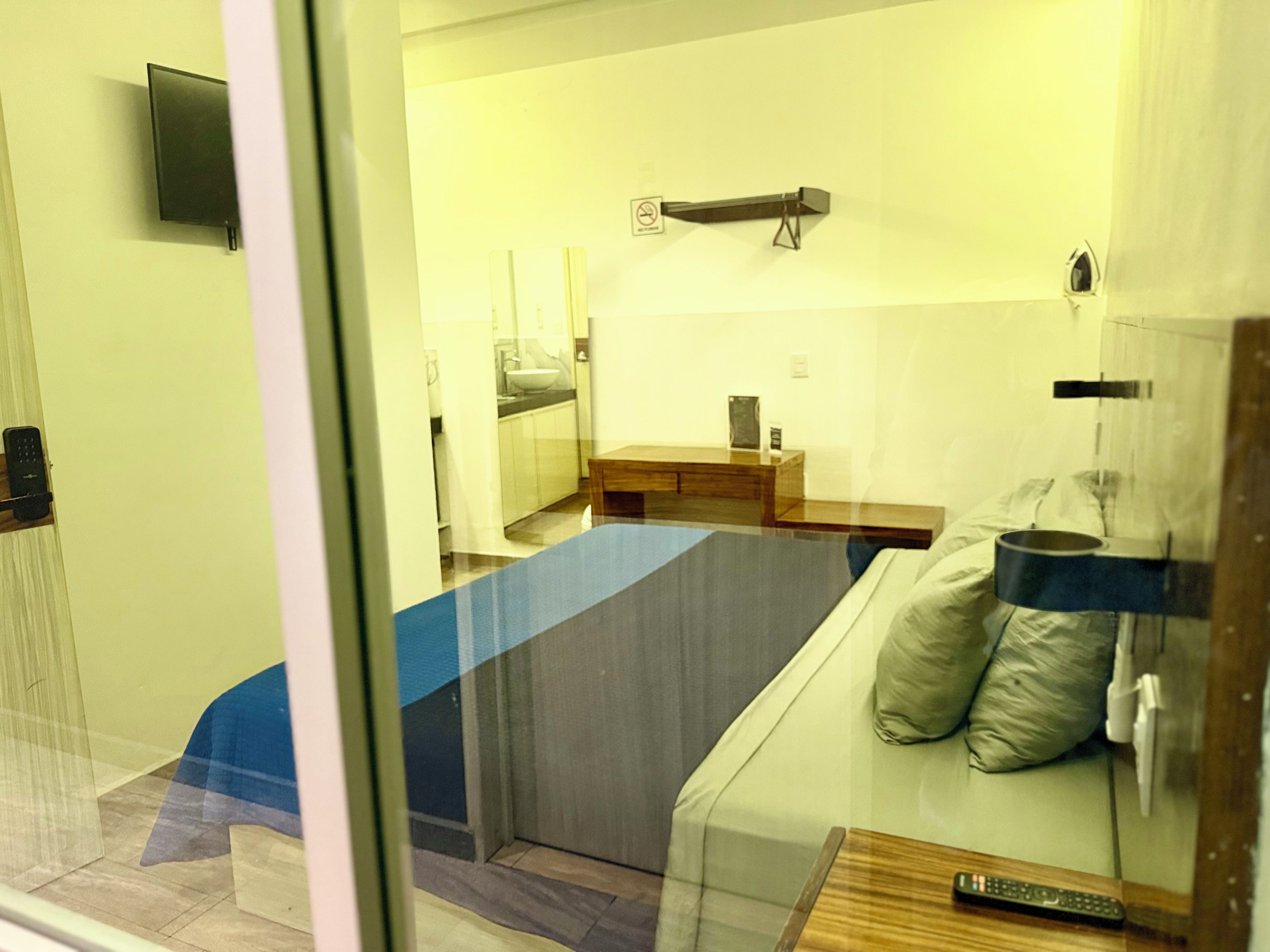 A hotel room with a bed, a bedside table, a remote control, and a view of the bathroom.