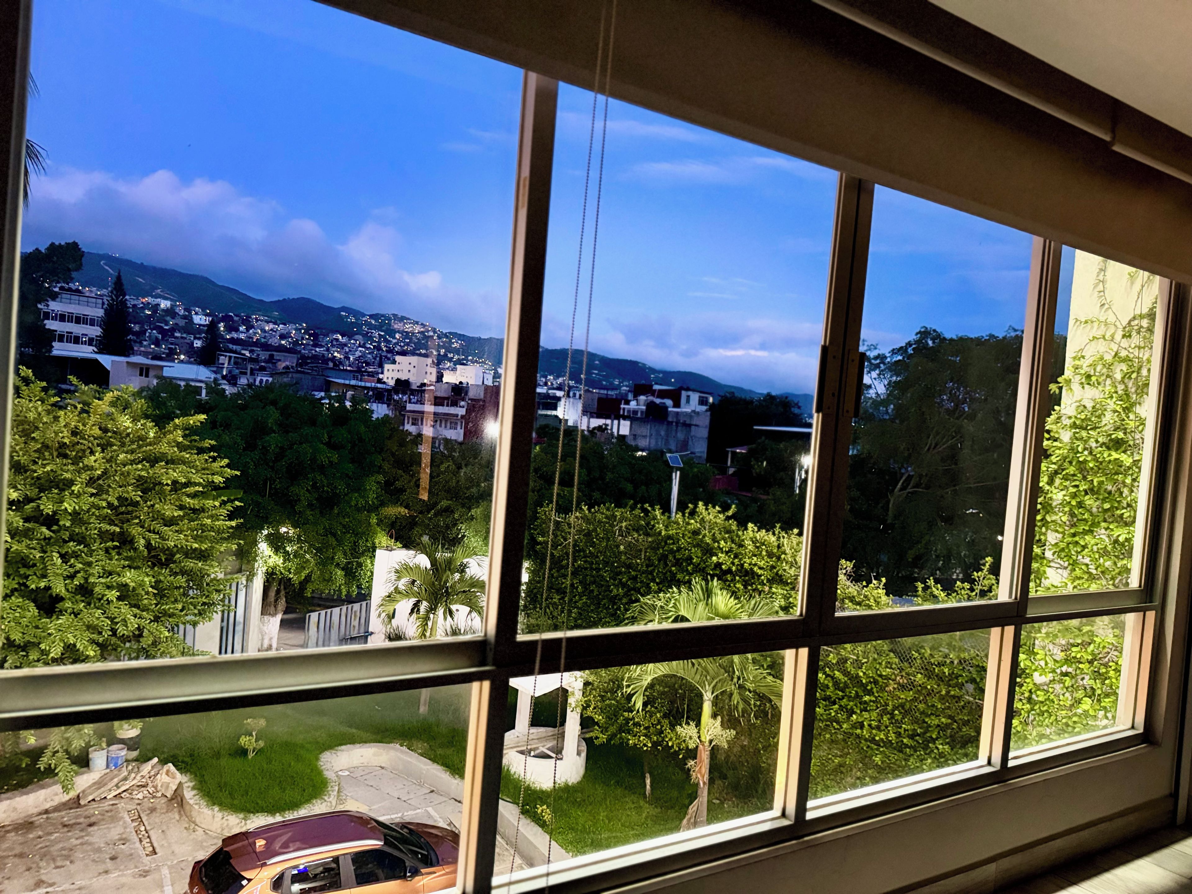 A room with a large window overlooking a residential area with houses and greenery.