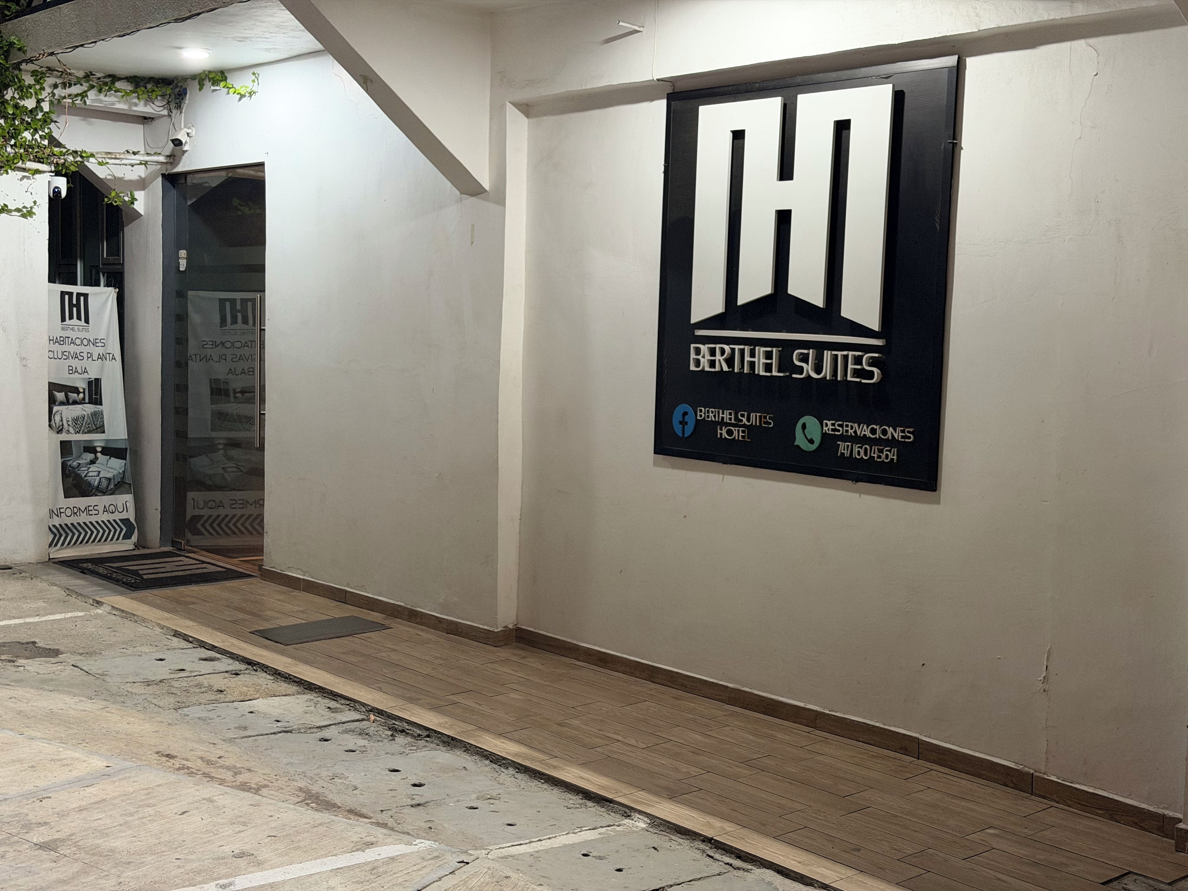 Corredor de hotel com uma grande placa para Berthel Suites, incluindo um número de telefone e ícones de redes sociais.