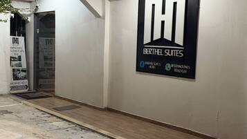 Corredor de hotel com uma grande placa para Berthel Suites, incluindo um número de telefone e ícones de redes sociais.