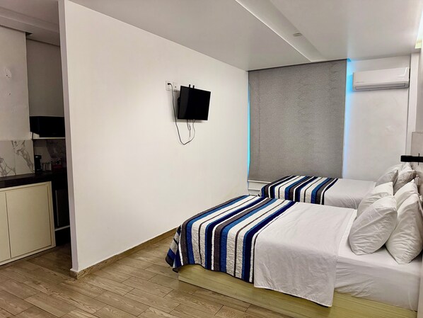 A modern hotel room with a flat-screen TV mounted on the wall, a grey headboard, and a bed with striped bedding.