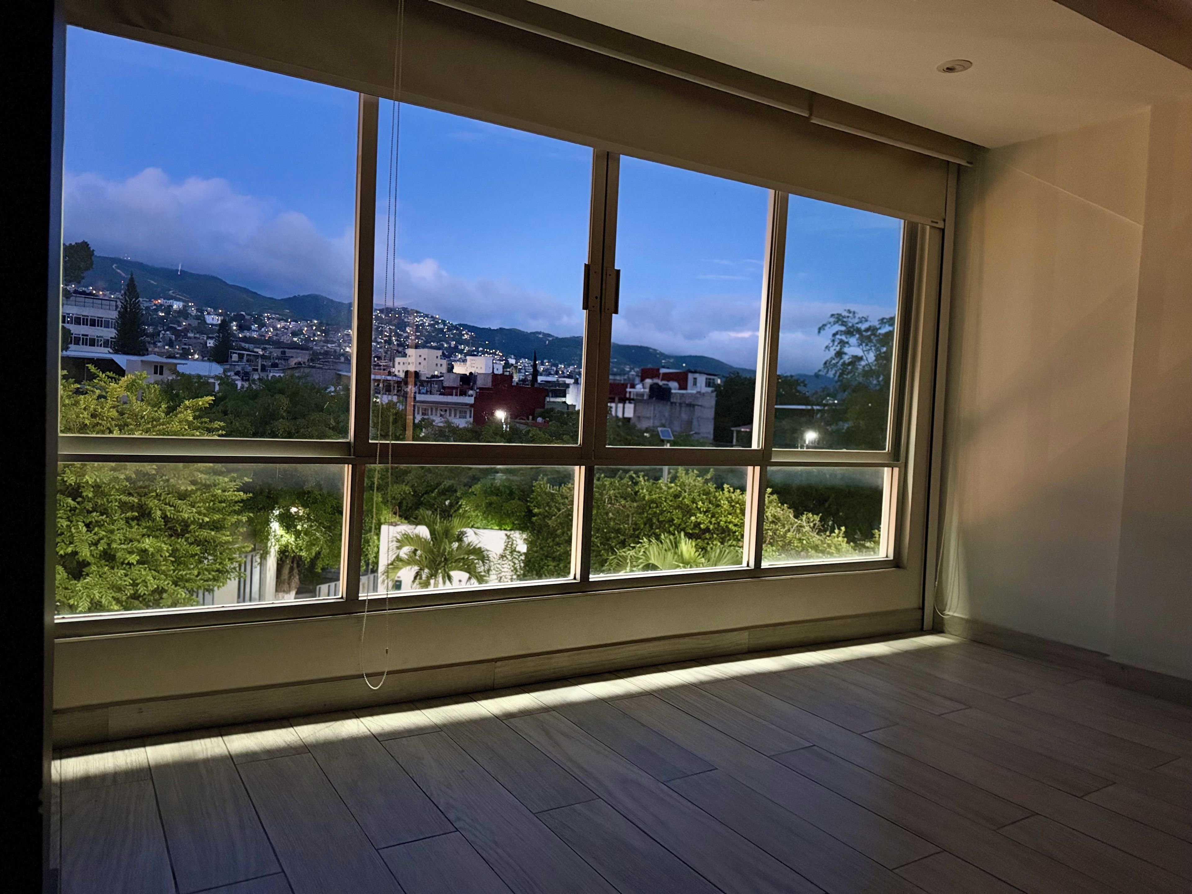 A room with a large window overlooking a cityscape at dusk.