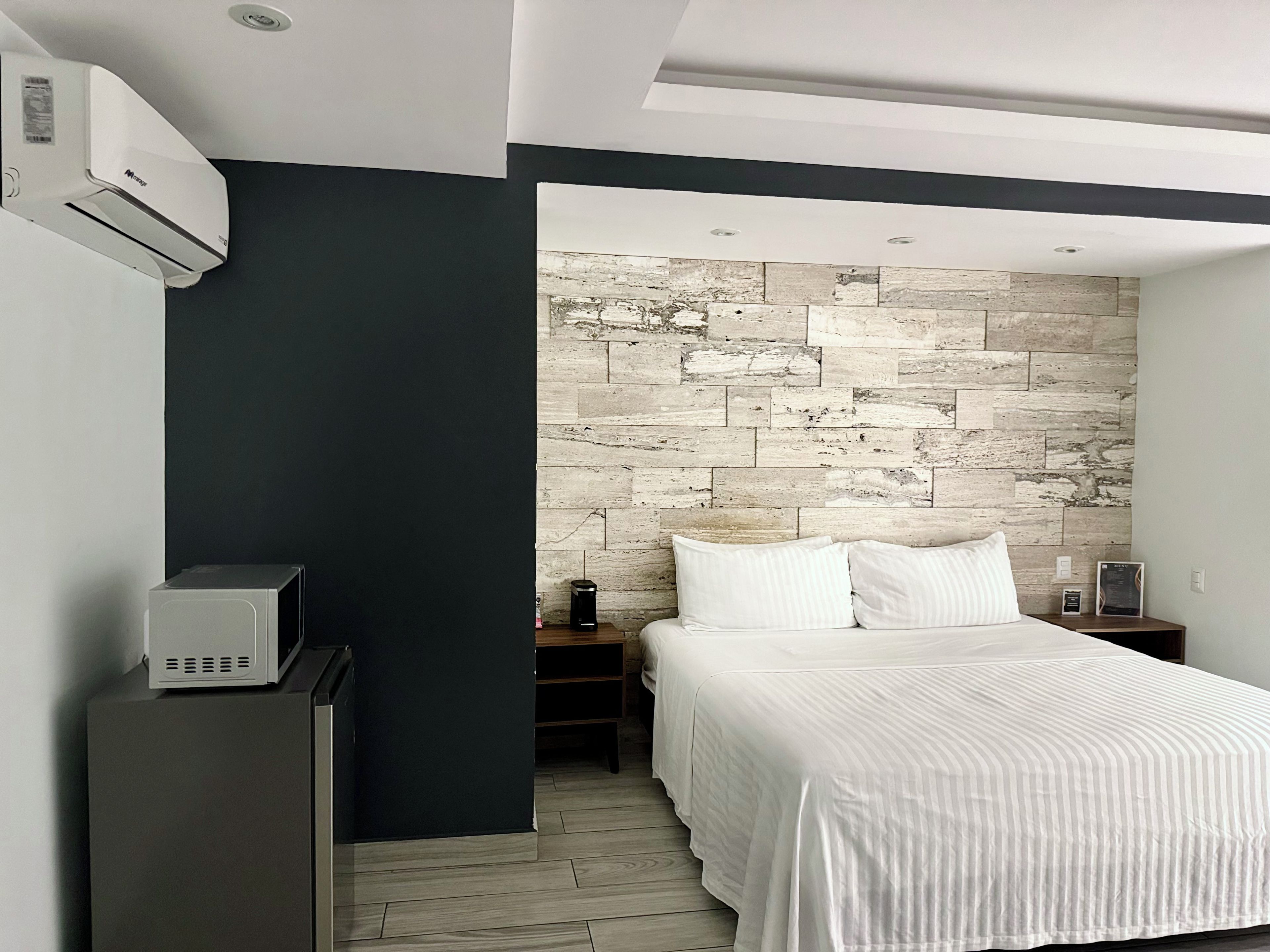 A modern bedroom with a bed, a nightstand, a dresser, and a wall-mounted air conditioner.