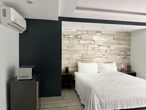 A modern bedroom with a bed, a nightstand, a dresser, and a wall-mounted air conditioner.