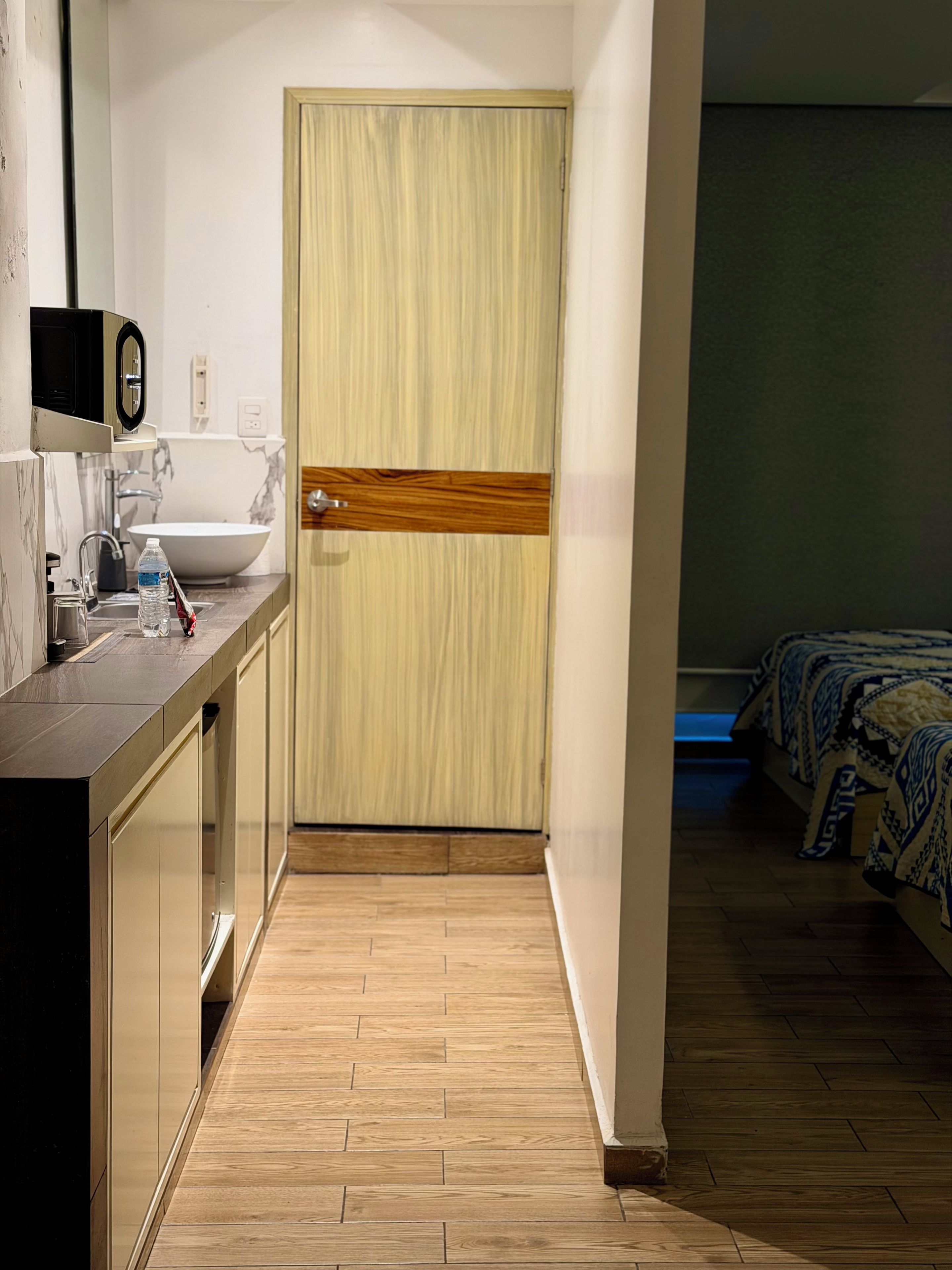 A hotel room with a wooden door, a sink, and a bed with patterned bedding.