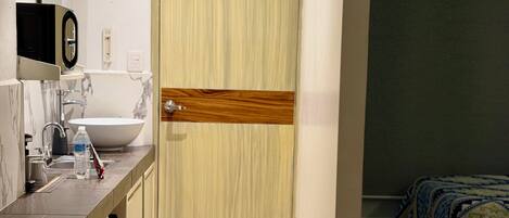 Een hotelkamer met een houten deur, een wastafel en een bed met beddengoed met een patroon.