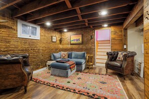 A cozy room with a brick wall, a blue sofa, leather armchairs, and a patterned rug. - West Highlands House Walk to Shops & Dining (Denver)