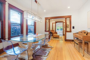 Un espace repas moderne avec une table à plateau en verre, des chaises transparentes et un piano en bois.