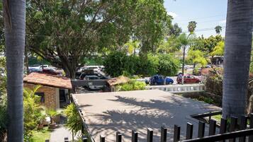 Un estacionamiento con varios coches, rodeado de árboles y un edificio con tejado de tejas.