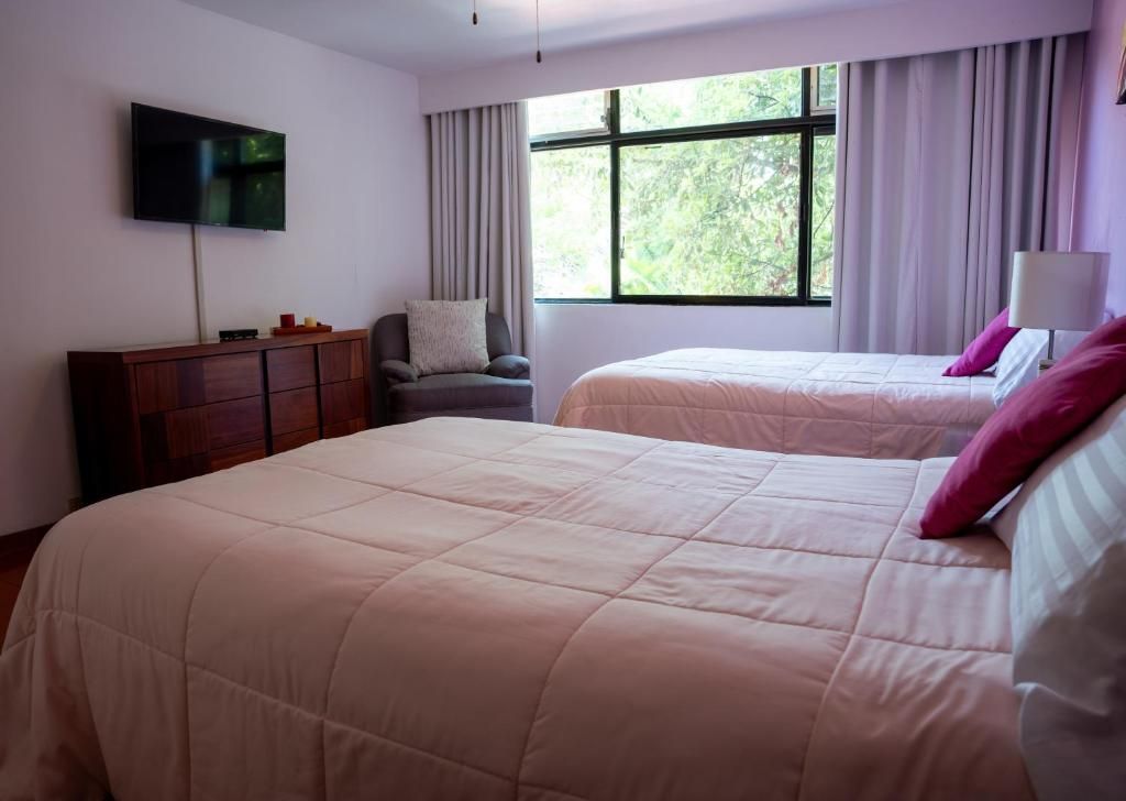 A hotel room with two beds, a TV mounted on the wall, a wooden dresser, and a window with curtains.