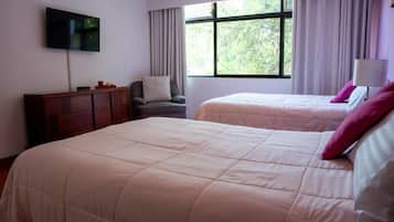 A hotel room with two beds, a TV mounted on the wall, a wooden dresser, and a window with curtains.