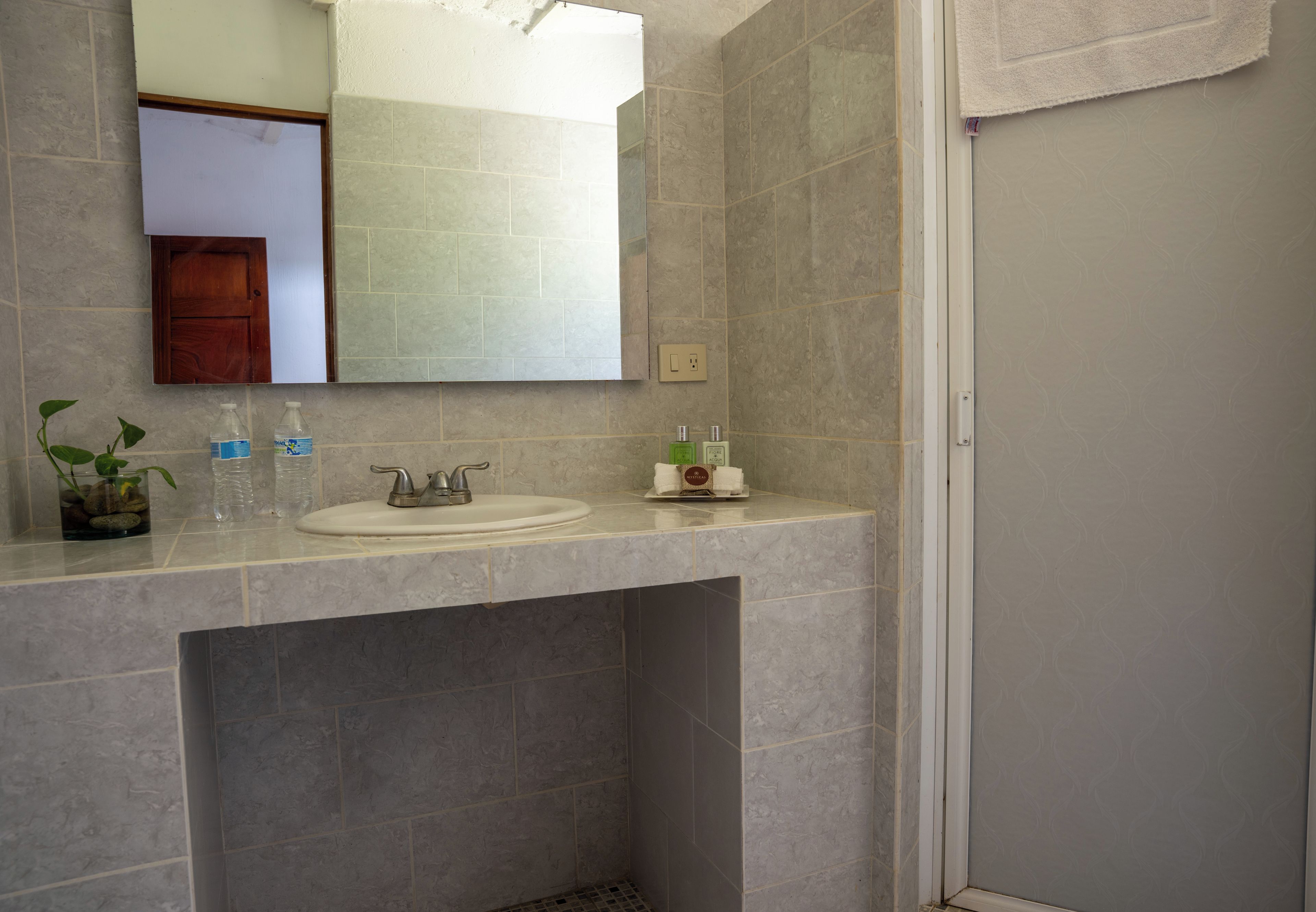 Baño con lavamanos, espejo y artículos de aseo.