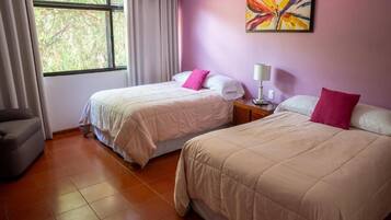 A hotel room with two beds, a window with curtains, a chair, and a painting on the wall.