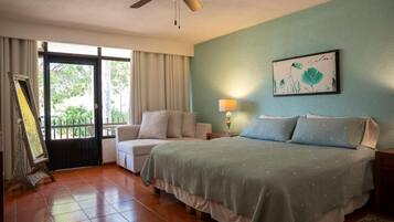 Habitación de hotel con cama, silla, mesita de noche, lámpara, ventilador de techo y ventana con cortinas.