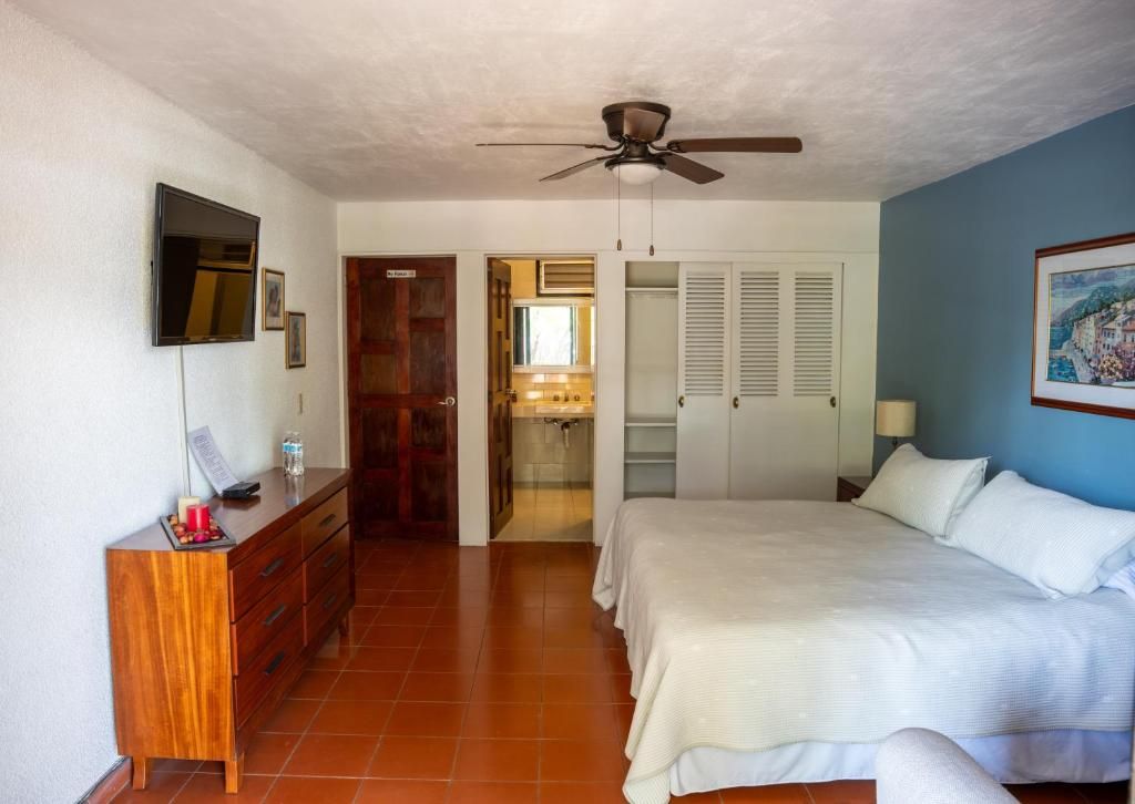Un dormitorio con cama, ventilador de techo, televisor en la pared y cómoda de madera.