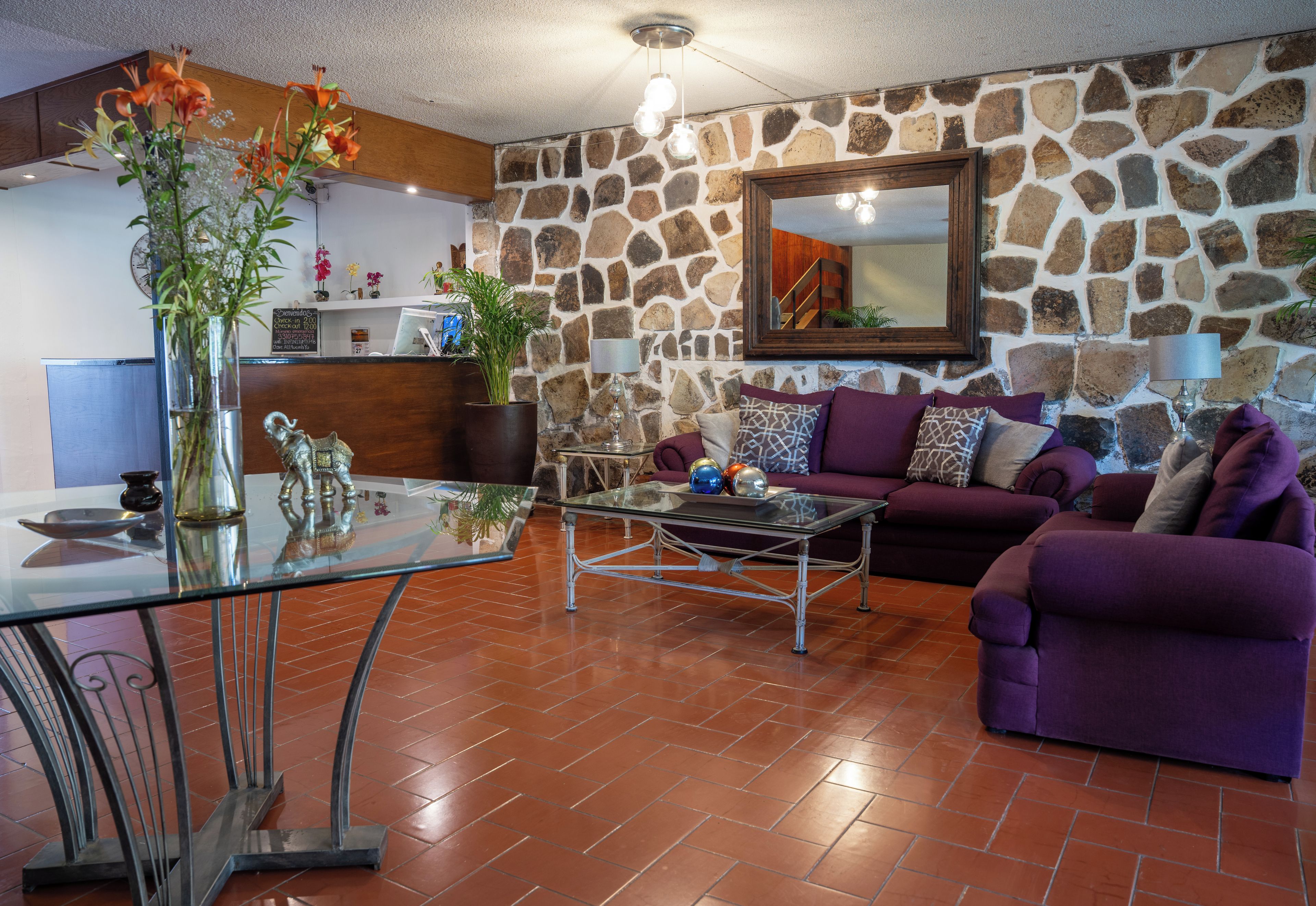 A living room with a stone wall, a glass coffee table, a purple sofa, and a reception desk with a clock.