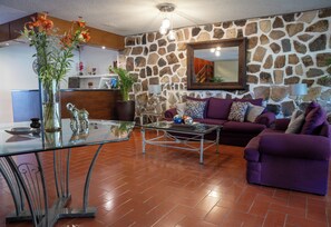 A living room with a stone wall, a glass coffee table, a purple sofa, and a reception desk with a clock. - HOTEL TOCA MADERA  (Chapala)