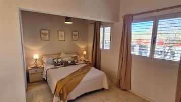 Un dormitorio con cama, lámparas de noche, un tapete circular y vistas al exterior por una ventana.