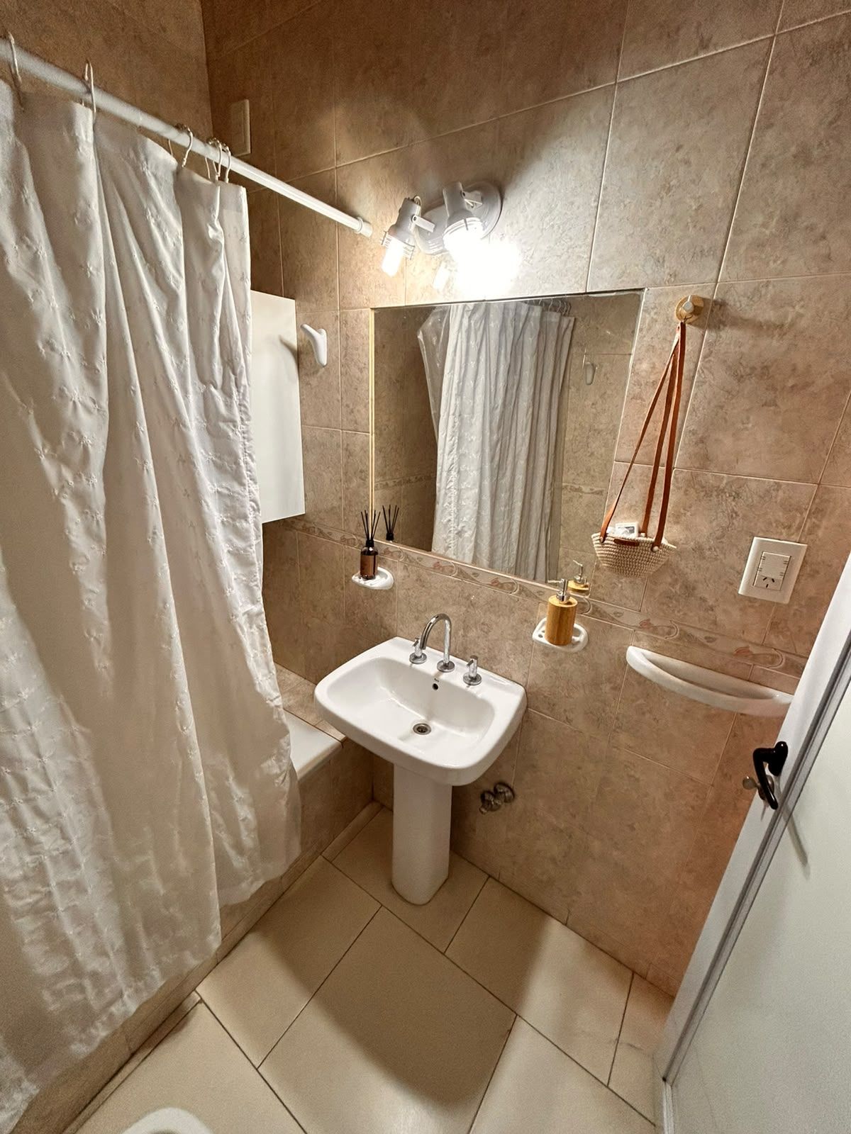 Un baño con lavamanos pedestal, cortina de ducha, espejo y toallero.