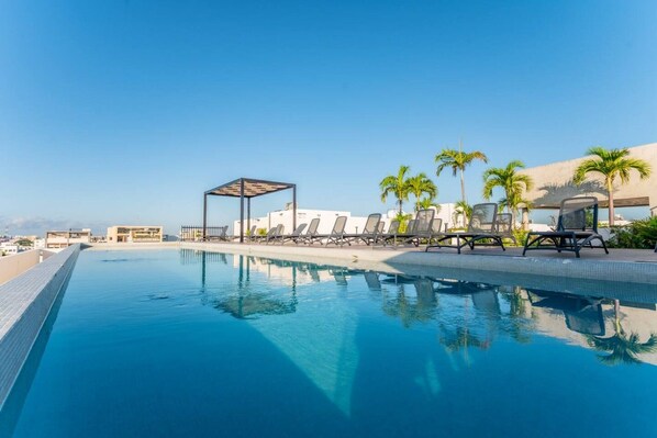 Une piscine entourée de palmiers, avec des chaises longues et une pergola.
