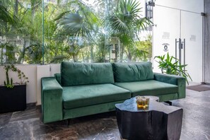 Ein grünes Sofa in einem Raum mit Glaswand, einem schwarzen Couchtisch und verschiedenen Pflanzen.