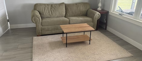 A living room with a sofa, a coffee table, a rug, and a window with a view.