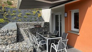 An outdoor patio with a table and chairs, a stone wall, and a covered area. - La Villa des Cimes (Pelleautier)