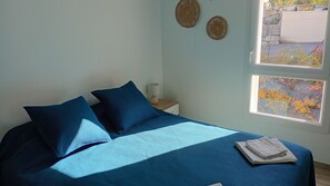 A bed with blue bedding, a nightstand with a lamp, and a window with a view of trees.