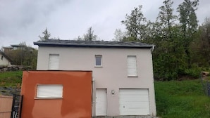 A two-story building with a garage door, a small window, and a door. - La Villa des Cimes (Pelleautier)