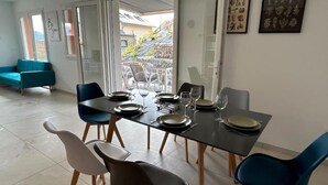 A dining area with a table set for four, chairs, and a view through a glass door. - La Villa des Cimes (Pelleautier)