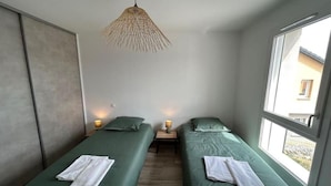 A room with two single beds, a hanging light fixture, a window, and a door. - La Villa des Cimes (Pelleautier)