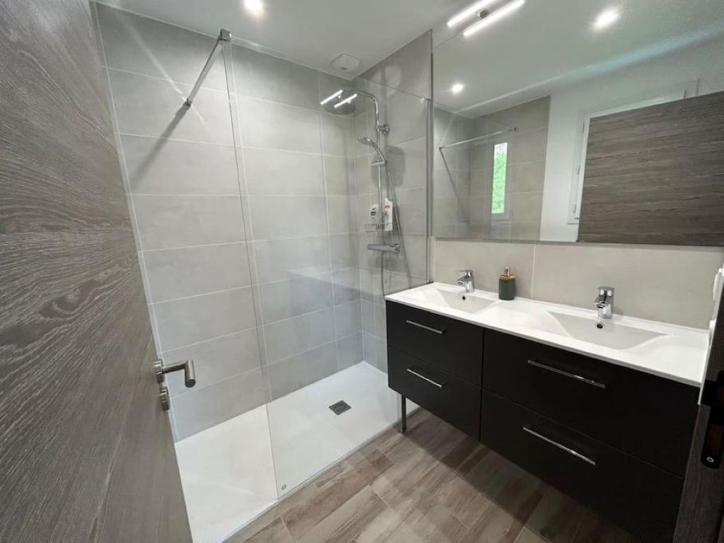 Un baño moderno con ducha de vidrio, lavamanos doble y un espejo grande.
