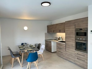 A modern kitchen with built-in appliances, a dining area with a table and chairs, and a light fixture on the ceiling. - La Villa des Cimes (Pelleautier)