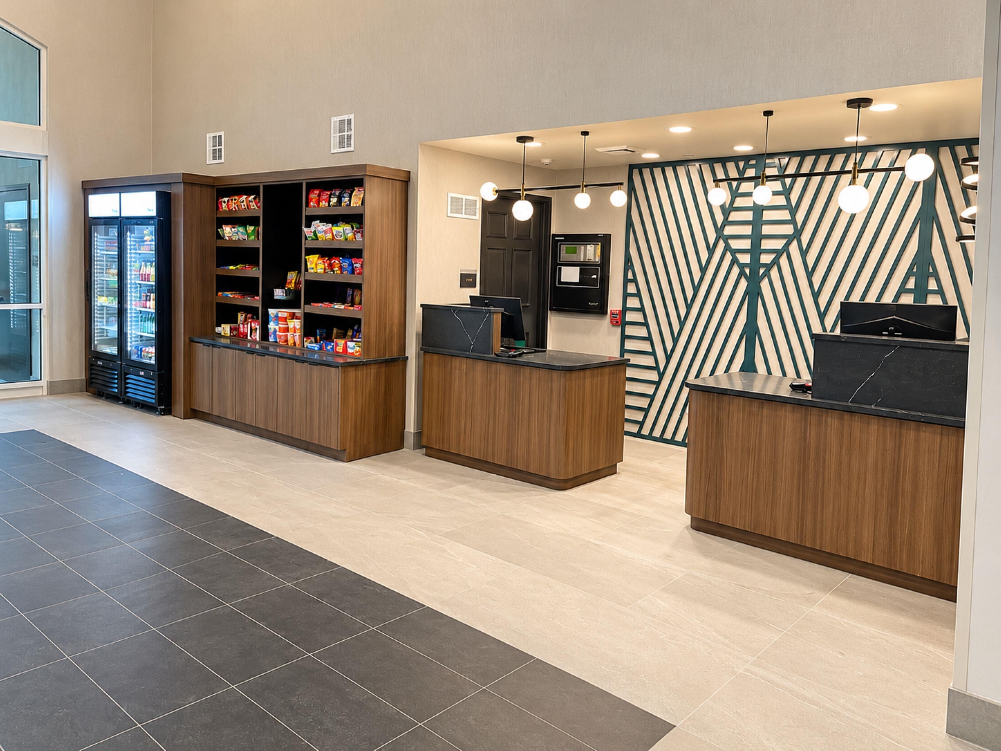 Zona de recepción con mostrador, un refrigerador lleno de bebidas y una pared con diseño.