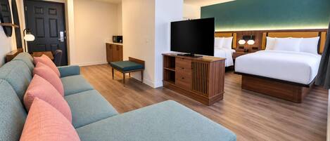 A hotel room with a sofa, a television, a bed, and a desk.