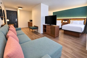 Et hotelværelse med sofa, fjernsyn, seng og skrivebord.