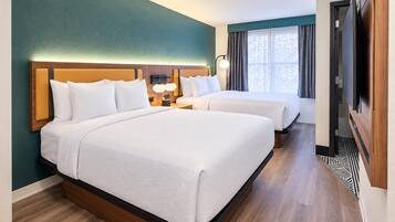 A hotel room with two beds, a wooden headboard, a nightstand with a lamp, and a window with curtains.