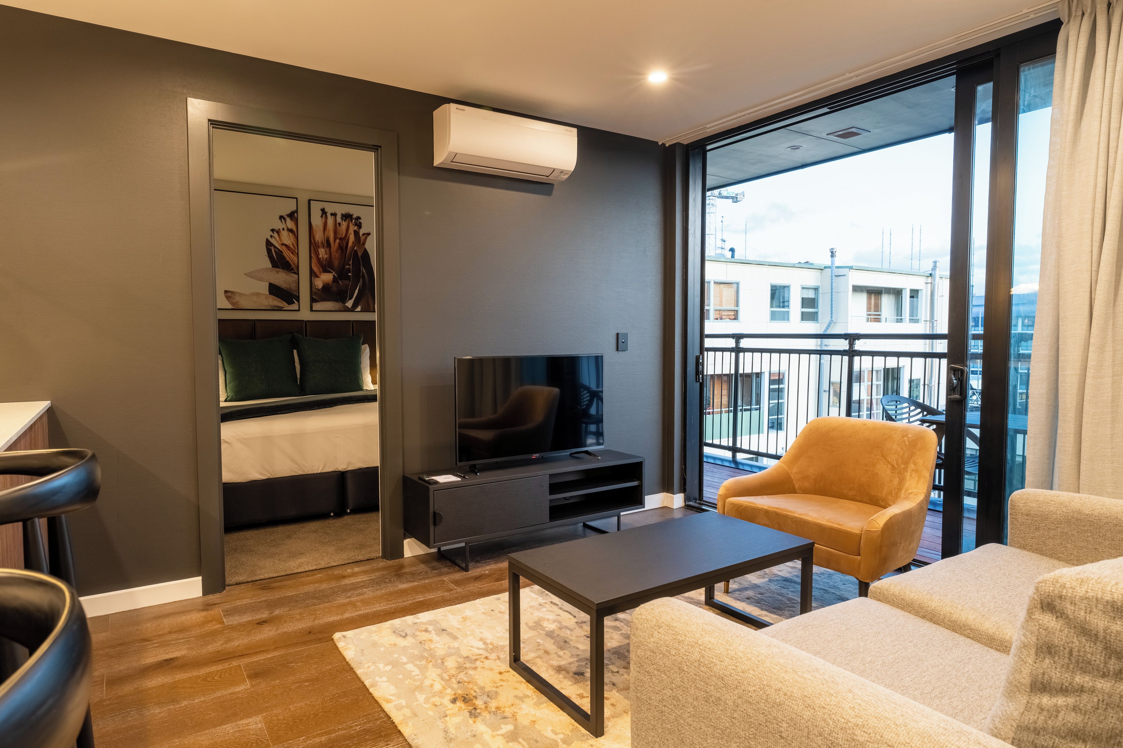 Una sala de estar moderna con un televisor de pantalla plana, un sofá, una mesa de centro y un balcón con vistas a edificios.