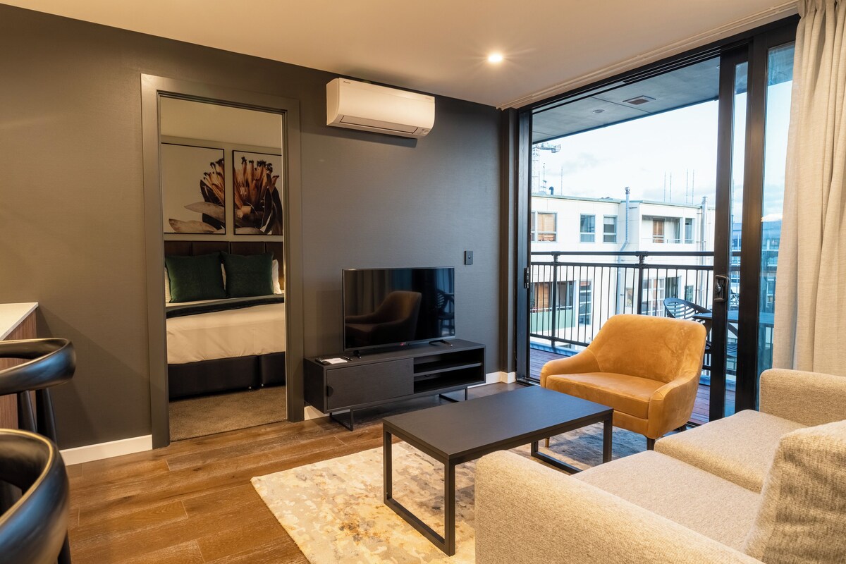 Una sala de estar moderna con un televisor de pantalla plana, un sofá, una mesa de centro y un balcón con vistas a edificios.