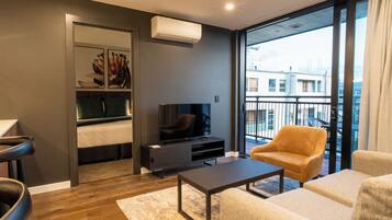 Una sala de estar moderna con un televisor de pantalla plana, un sofá, una mesa de centro y un balcón con vistas a edificios.