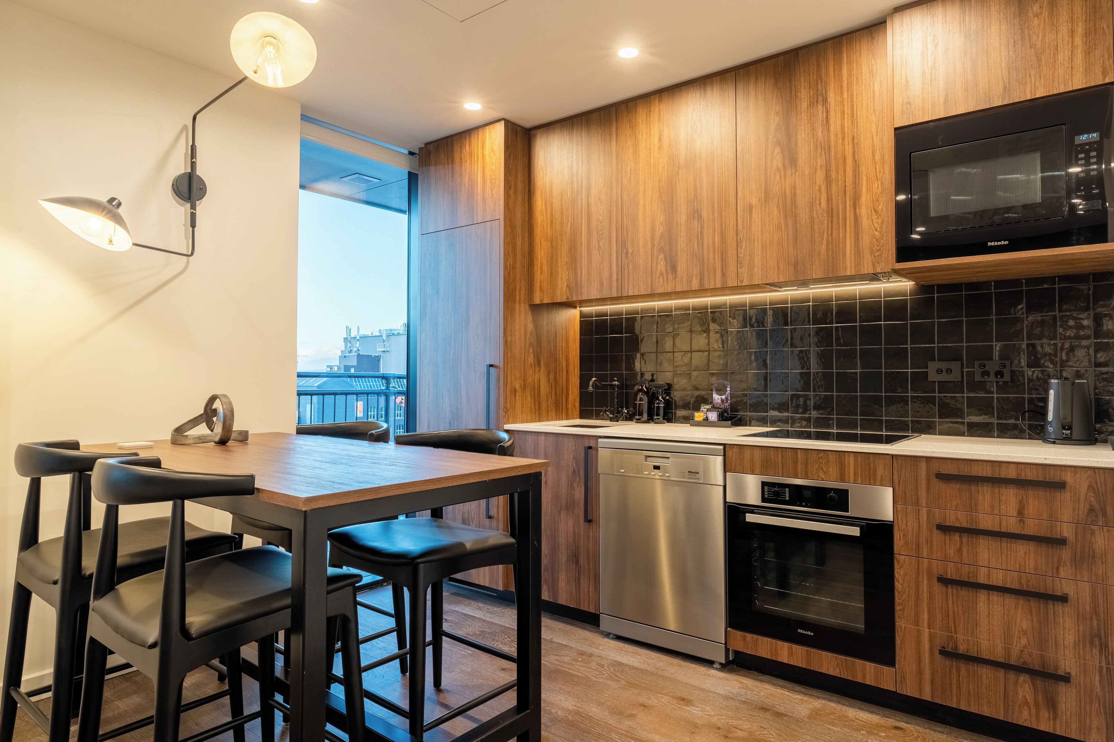 A modern kitchen with wooden cabinets, a built-in microwave, a dishwasher, and a dining area with a table and chairs.