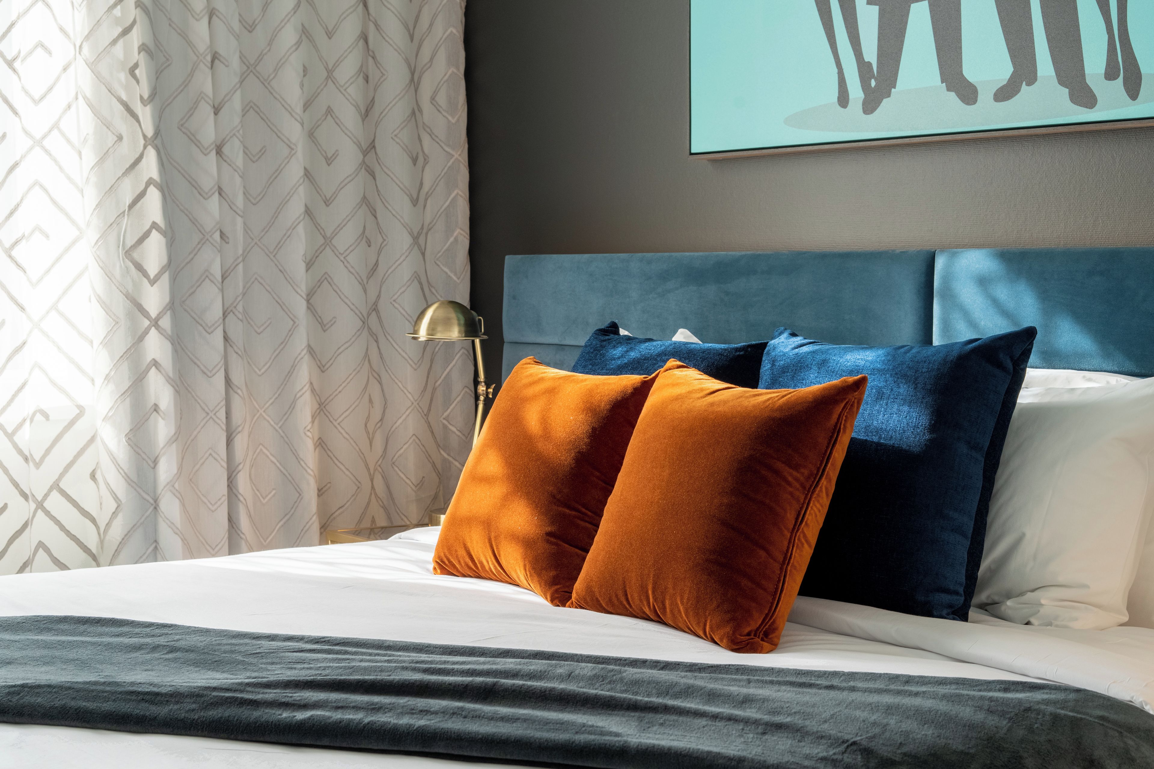A neatly made bed with a blue headboard, two pillows, and a grey blanket.