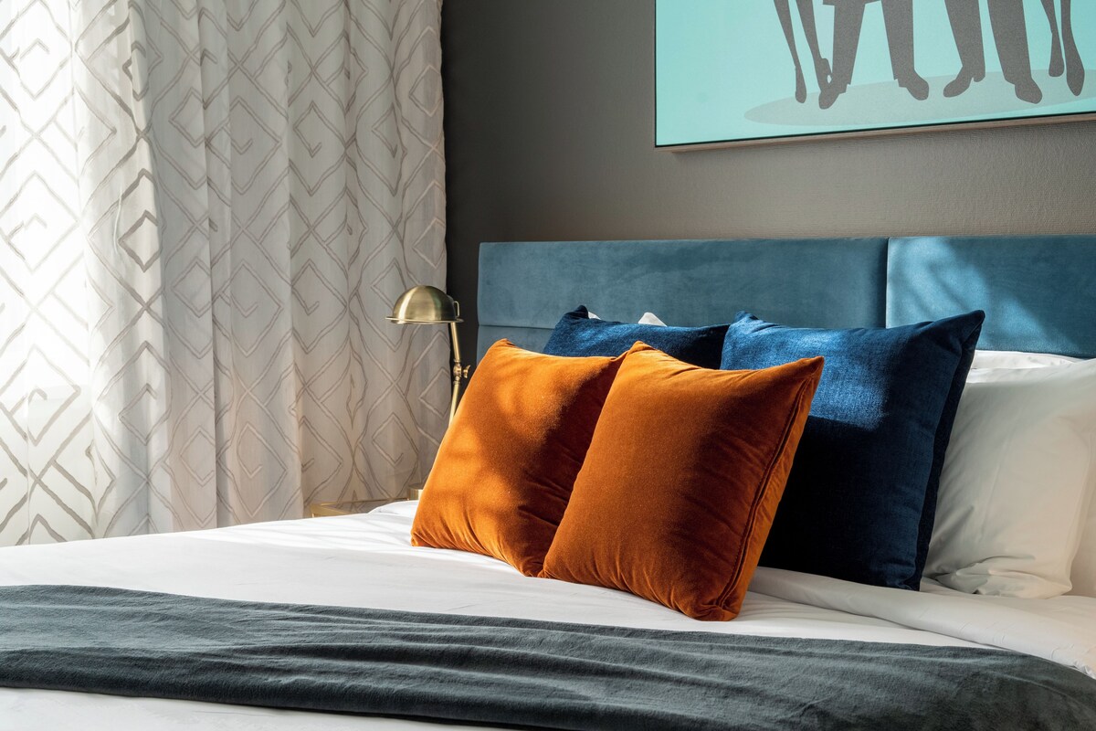 Una cama bien hecha con un cabecero azul, dos almohadas y una manta gris.