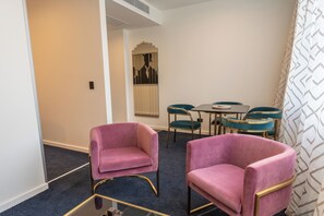 Habitación de hotel con dos sillones rosados, una mesa redonda y sillas color turquesa.