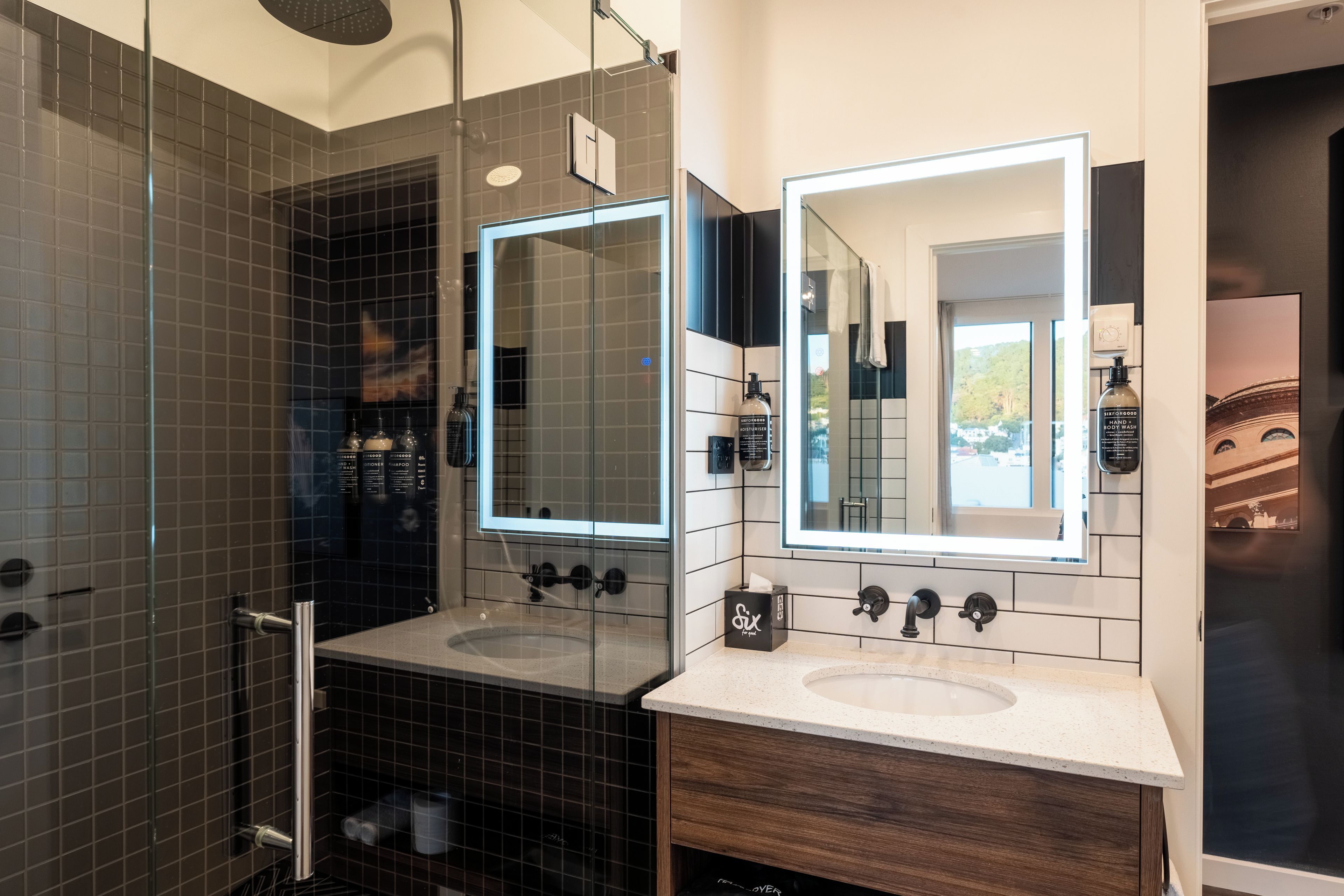 A modern bathroom with two sinks, a glass shower enclosure, and a large mirror.