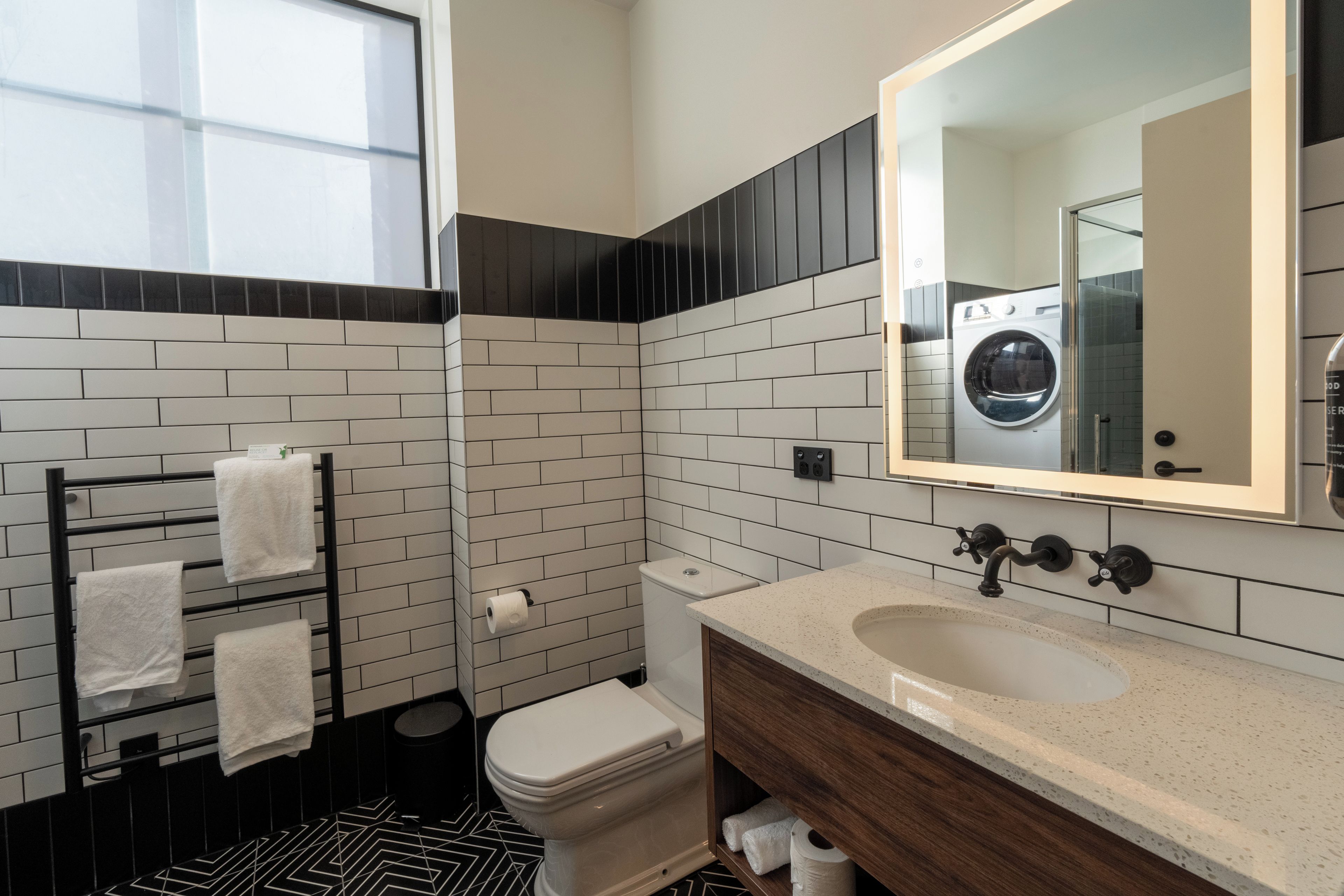 A modern bathroom with a black and white tiled wall, a white toilet, a sink with a mirror, and a towel rack.