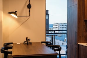 Un comedor moderno con una mesa y sillas de madera, una lámpara colgante y vistas a edificios a través de una ventana.