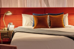 Una habitación de hotel con una cama, una lámpara de noche, un teléfono y un cabecero rojo.