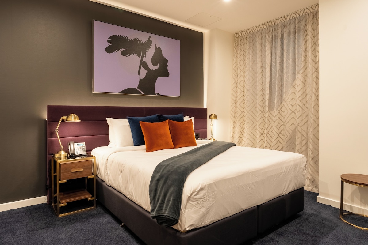 Una habitación de hotel con una cama grande, una mesita de noche con un teléfono y una obra de arte colgada en la pared.